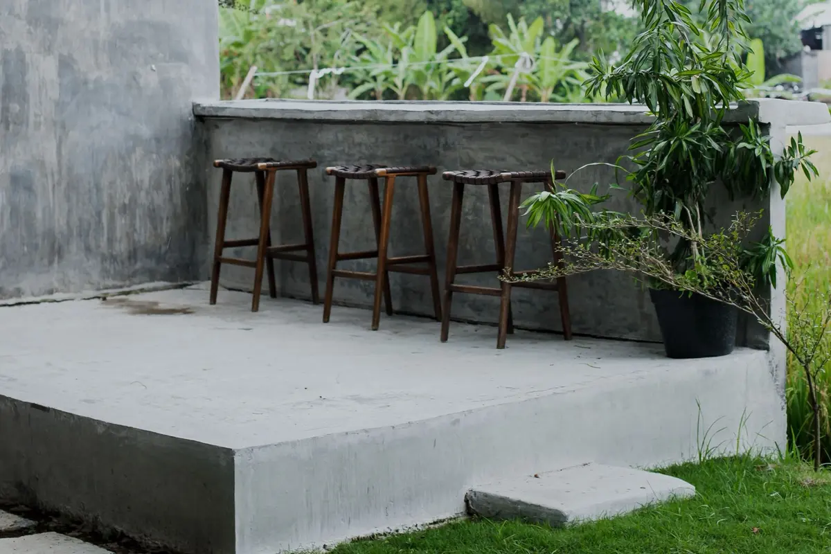 Raised concrete patio slab with bar stools along a low concrete wall