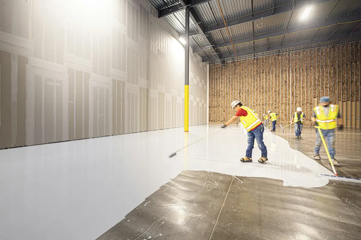 Crew rolling a white epoxy coating onto a bare concrete floor